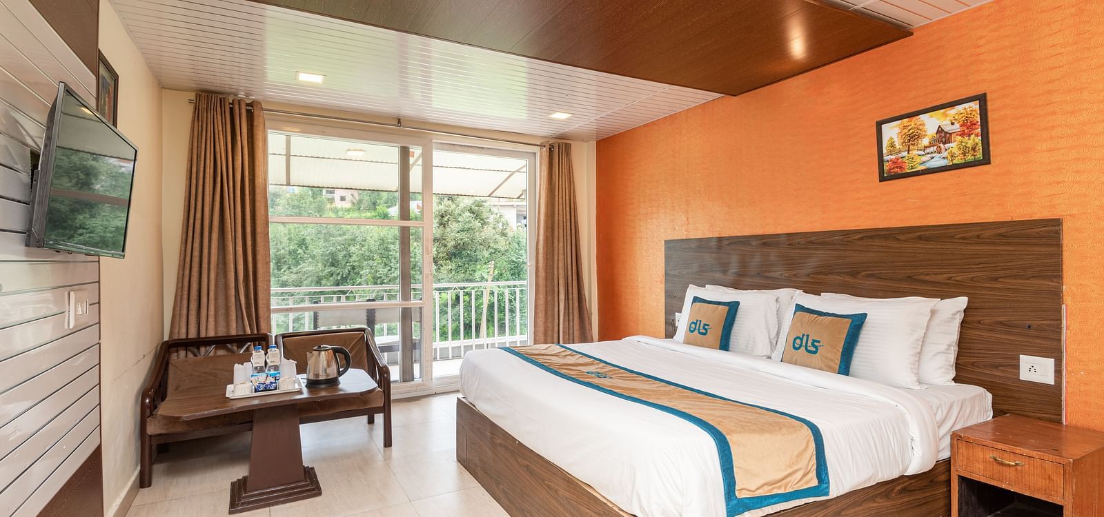 Shot of a room with king size bed, orange wall, private balcony and a side table | DLS Anupam Resort, Dharamshala